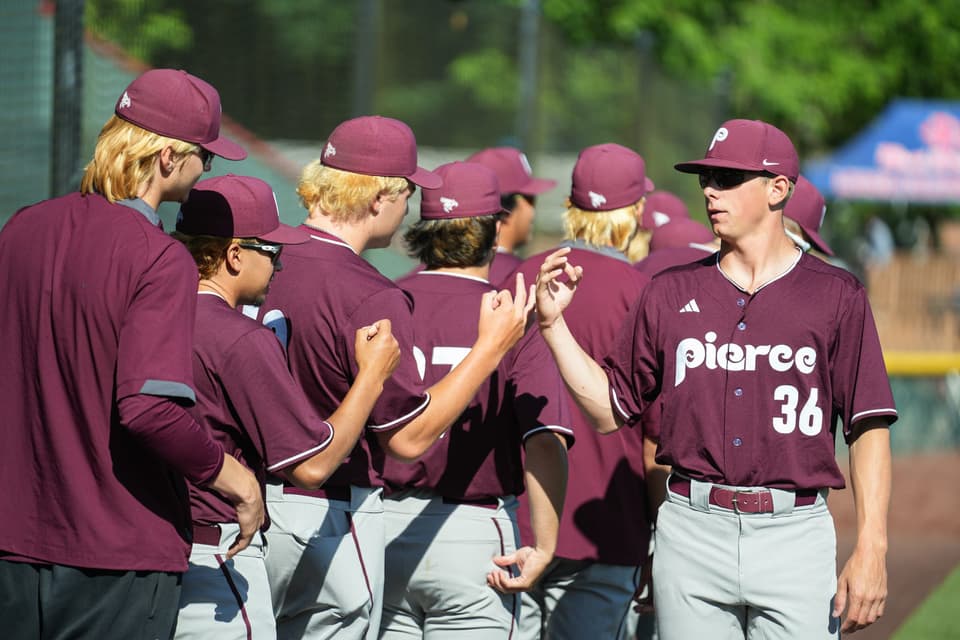Pierce baseball players in maroon uniforms gathering beside the field at the NWAC Championship