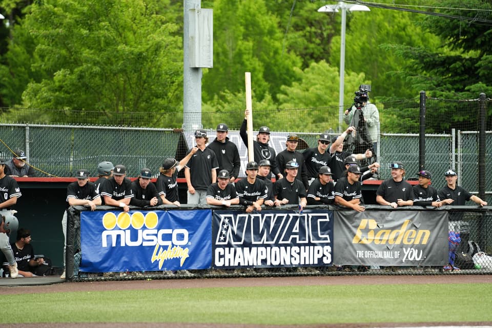 Lower Columbia players watching the field from behind an NWAC Championships banner