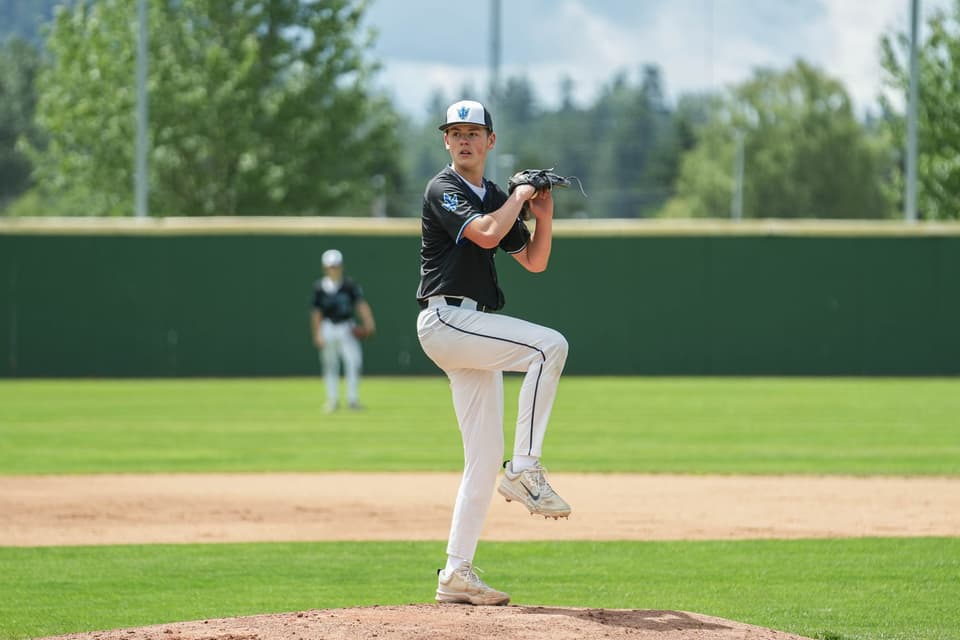 Baseball pitcher in a dark jersey lifting his knee into a windup at the 2026 Showcase