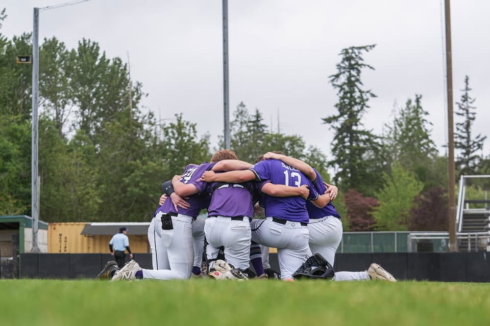 Baseball players in purple jerseys gathering in a team huddle at the 2026 Showcase